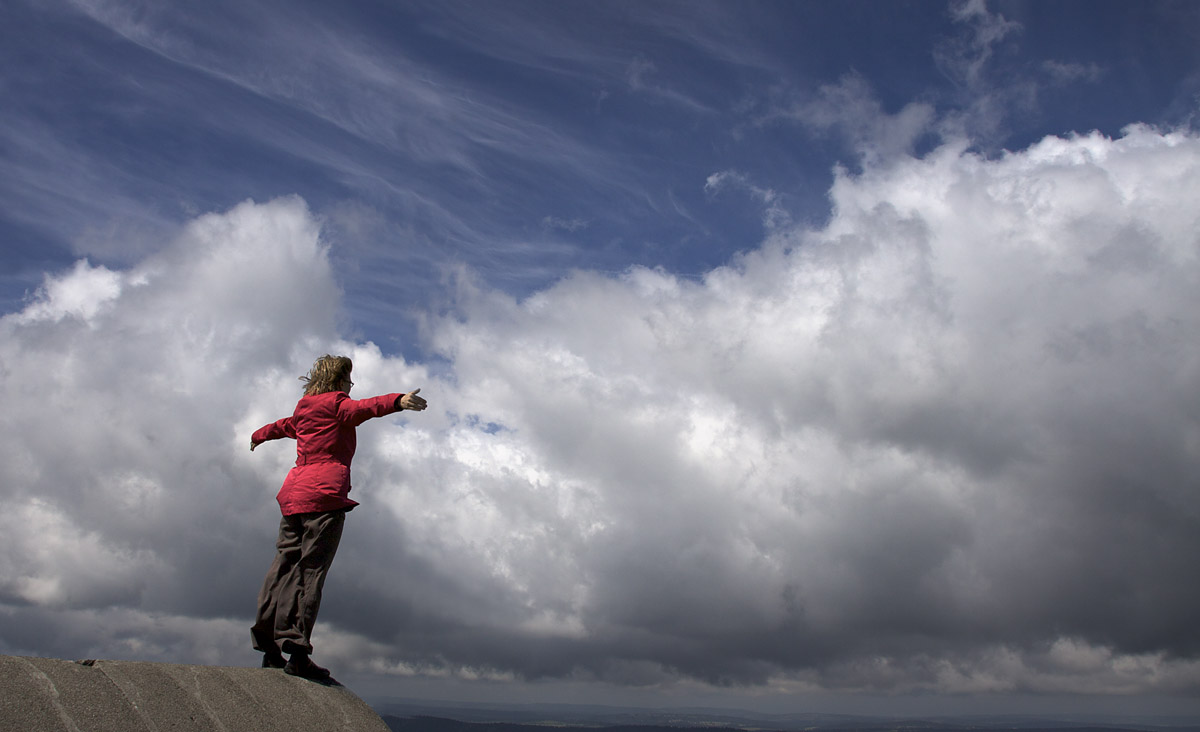 Eine Frau streckt die Arme aus und sieht aus, als ob sie die Wolken vor ihr umarmen würde. Ein Bild von Aufbruch und Freiheit